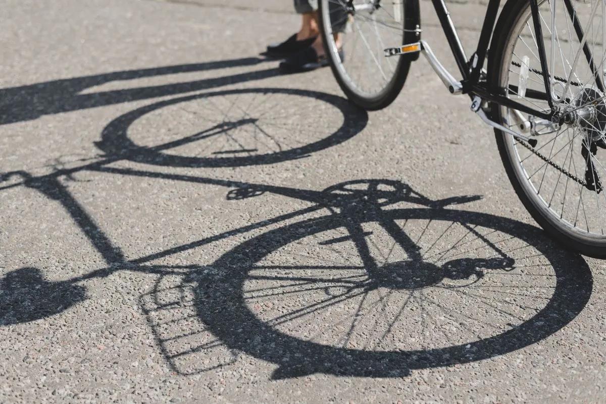 Bicicleta negra y su sombra sobre el asfalto, con los pies de un ciclista detenido al fondo