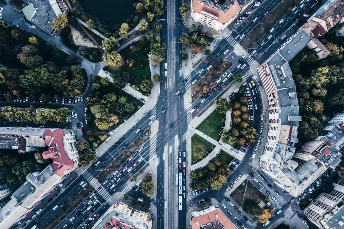 Vista aérea de un cruce de avenidas con autos, árboles y edificios de techos rojos