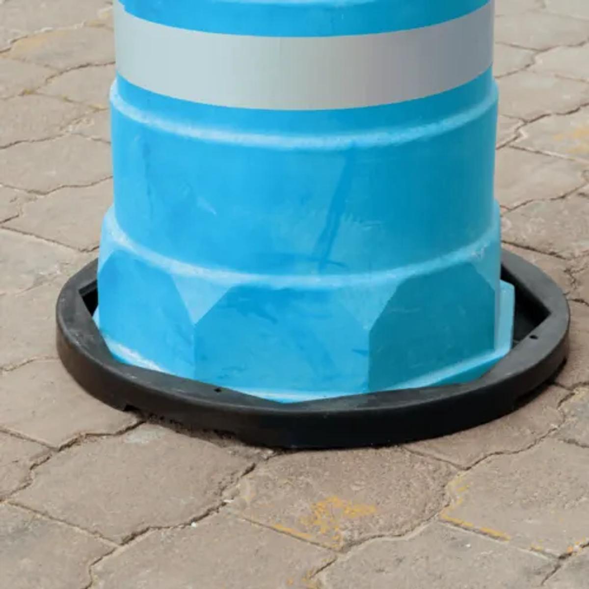 Trafitambo azul claro con banda reflejante blanca montado en una base negra sobre piso de adoquín
