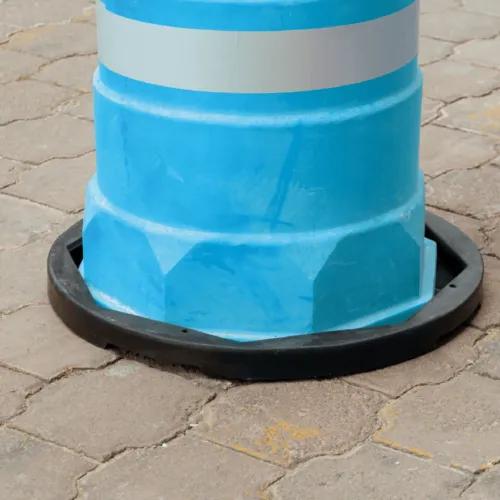 Trafitambo azul claro con banda reflejante blanca montado en una base negra sobre piso de adoquín