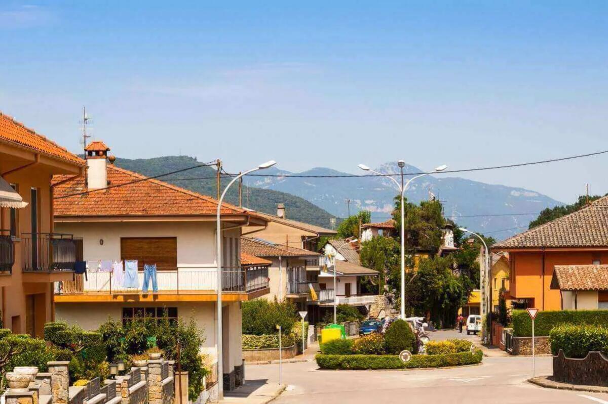 Calle residencial con casas de techo de teja, postes de luz y una glorieta con setos, con montañas al fondo