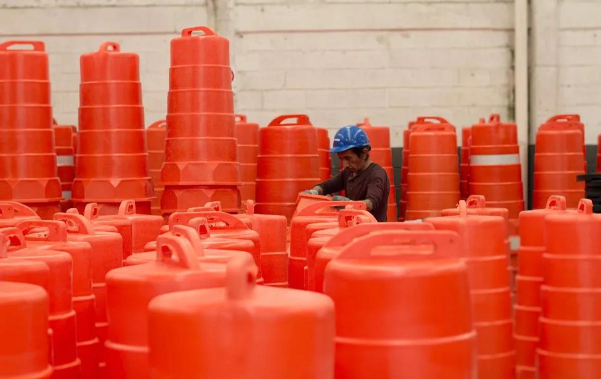 Trabajador con casco azul revisa trafitambos naranjas con asa entre decenas de piezas dentro de una nave