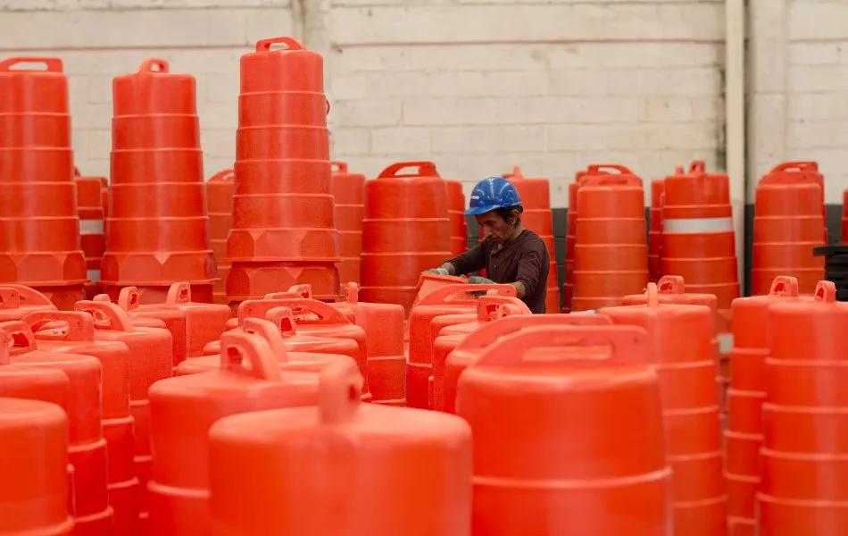 Trabajador con casco azul revisa trafitambos naranjas con asa entre decenas de piezas dentro de una nave
