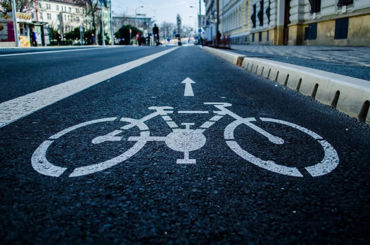 Carril para bicicletas con el símbolo de bici y una flecha pintados en blanco junto a una guarnición con separadores