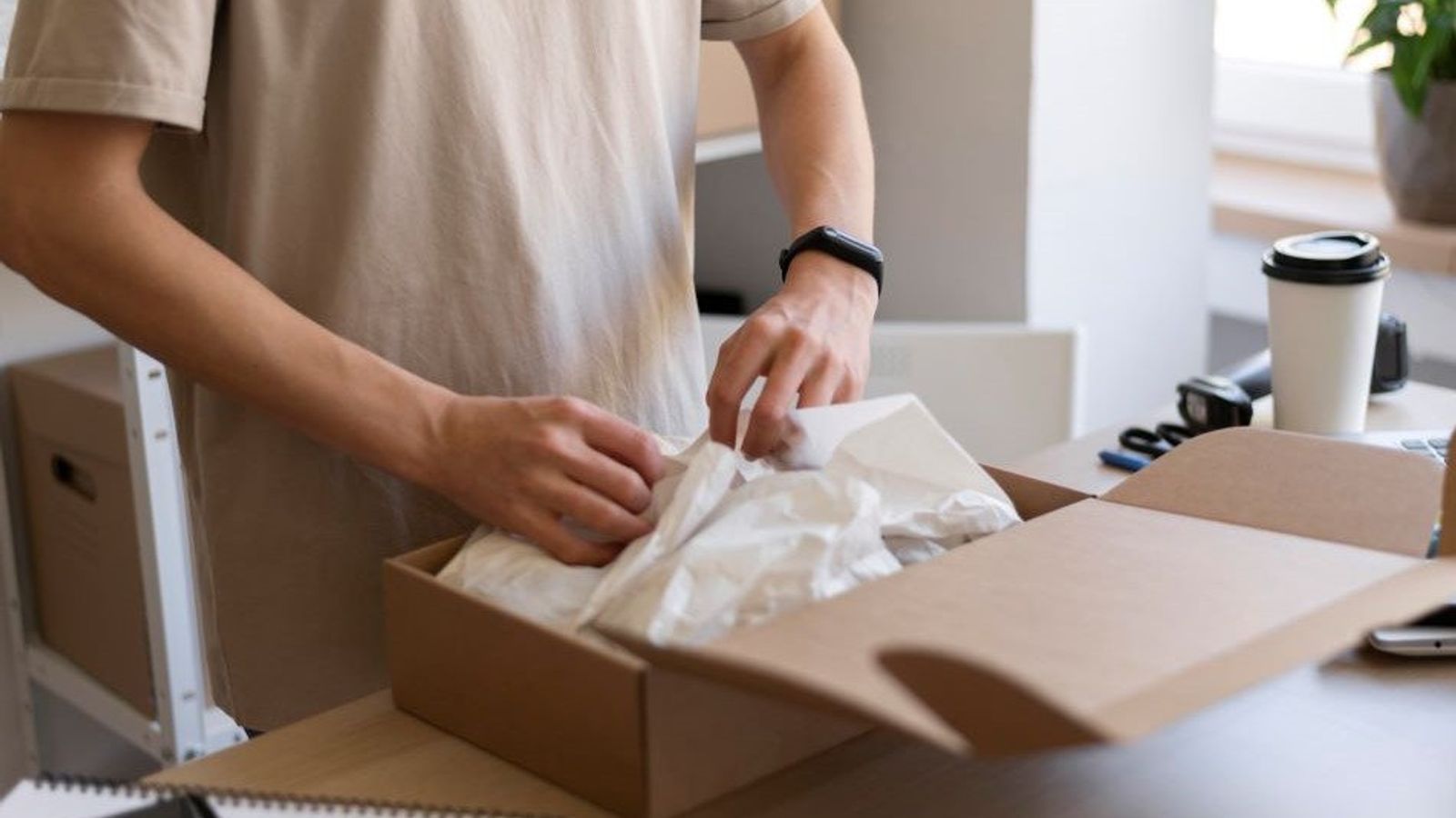 Persona acomoda papel de seda blanco dentro de una caja kraft pequeña sobre un escritorio