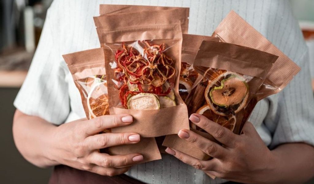 Manos sostienen bolsas de papel kraft con ventana transparente llenas de fruta deshidratada