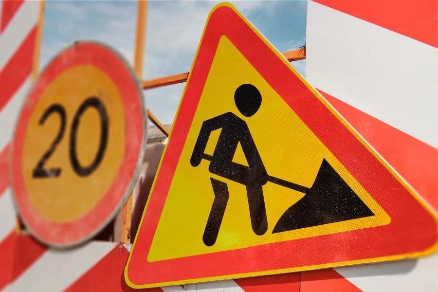 Señal triangular de hombres trabajando y señal redonda de límite 20 junto a barreras rayadas rojo con blanco en una obra
