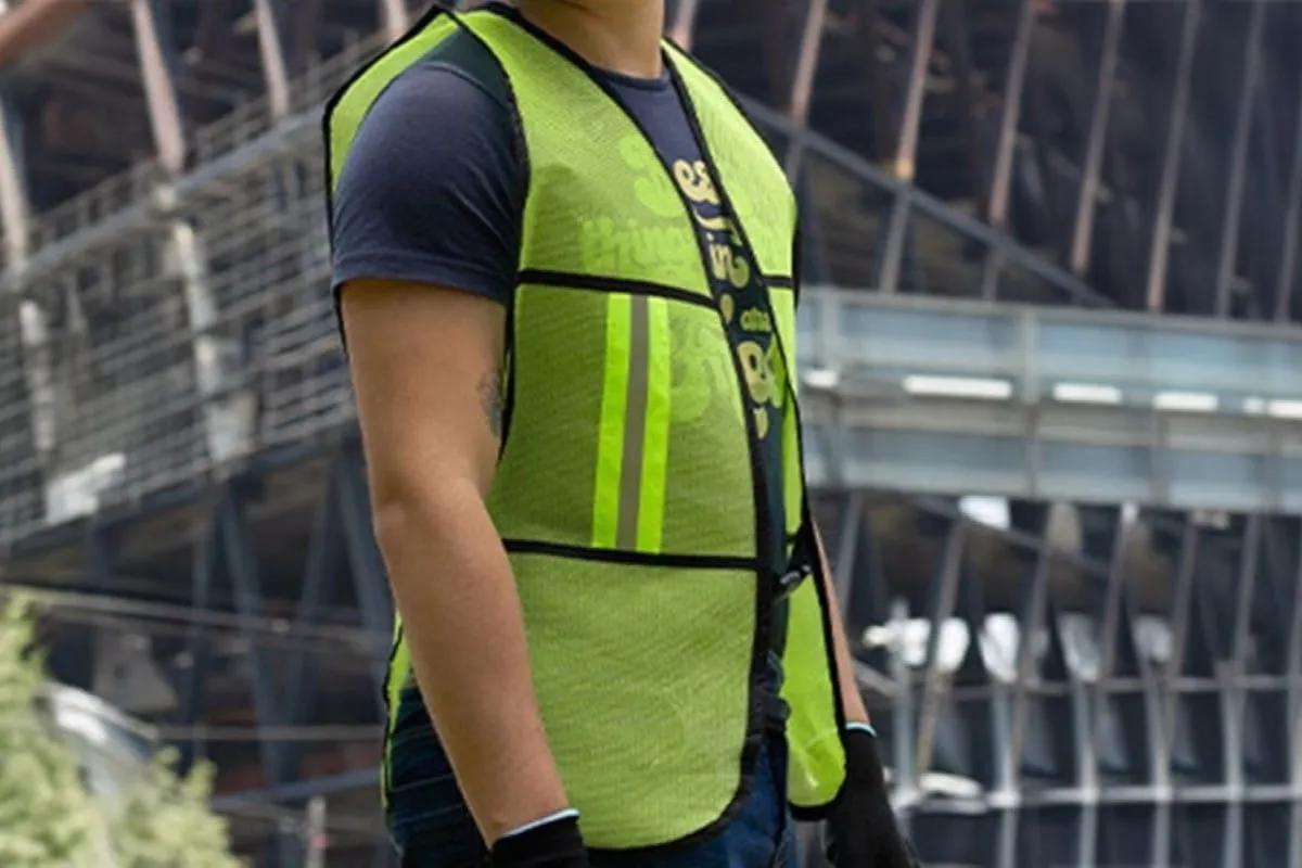 Trabajador con chaleco de seguridad verde neón con franjas reflejantes frente a una estructura de acero en obra