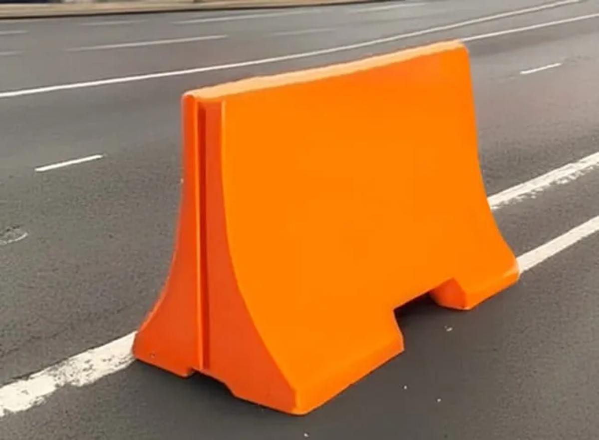 Barrera plástica naranja tipo New Jersey, sin reflejantes, sobre el carril de una avenida
