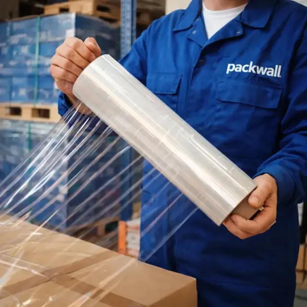 Operador con uniforme azul de Packwall sostiene un rollo de playo (stretch film) frente a tarimas emplayadas