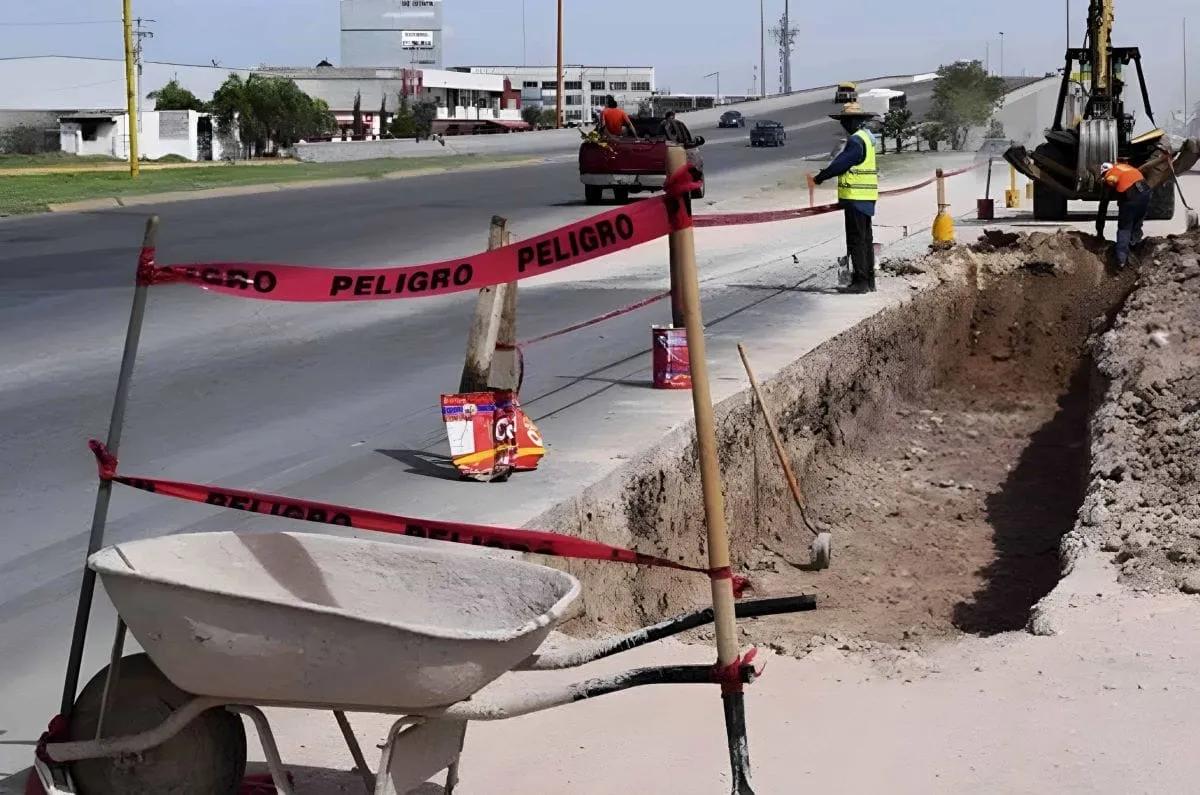 Cinta roja de PELIGRO sujeta a estacas alrededor de una zanja en obra, con una carretilla al frente