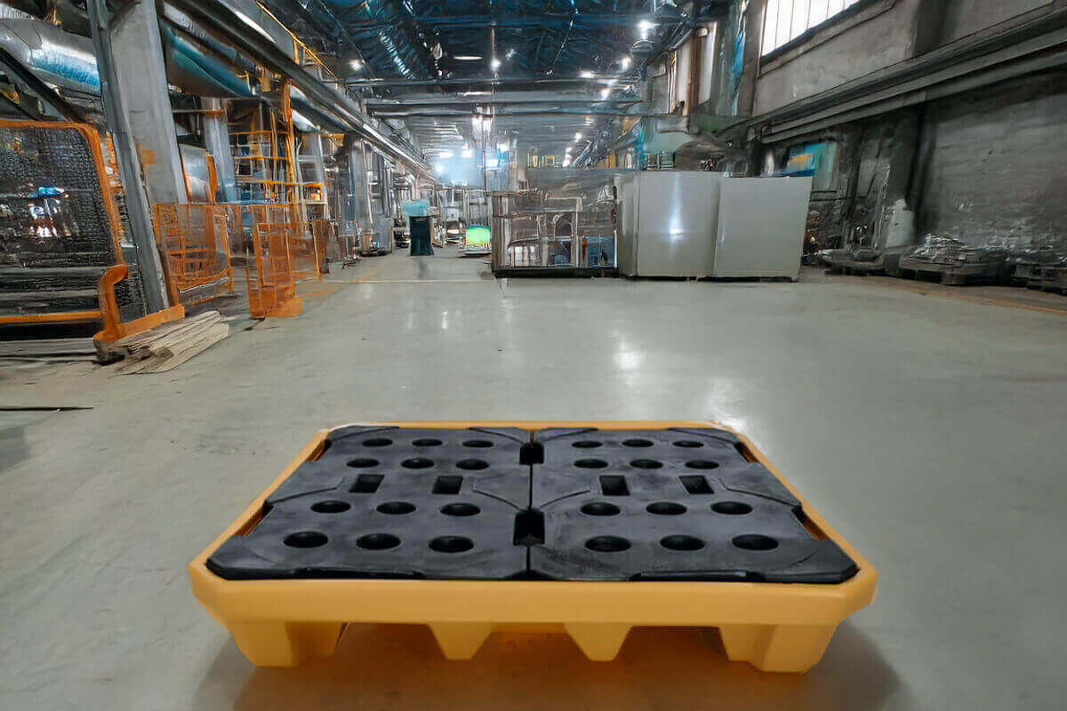 Tarima antiderrame amarilla con rejilla negra colocada en el piso de una planta industrial