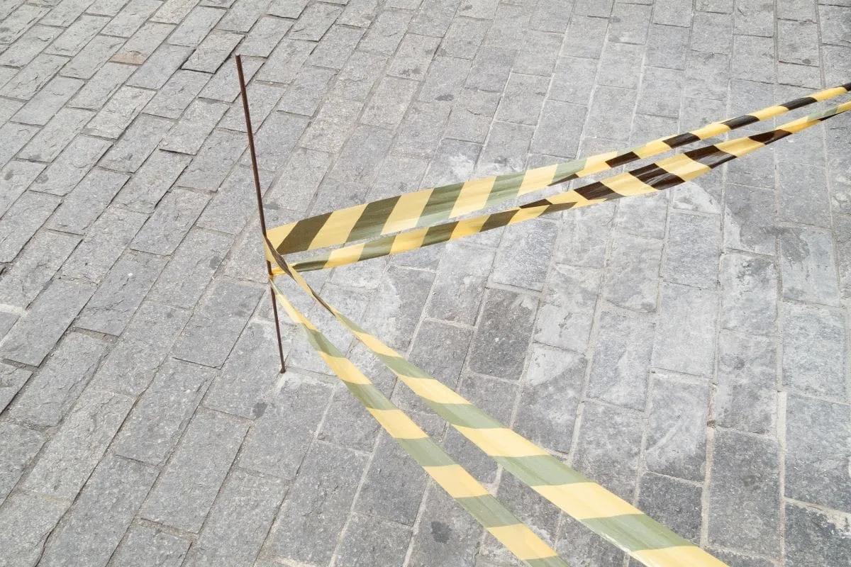 Cinta de precaución amarilla y negra amarrada a una varilla sobre piso de adoquín