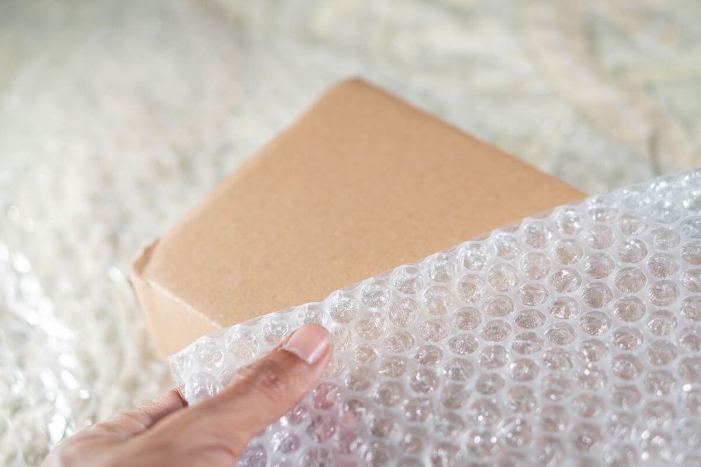 Mano extiende una lámina de poliburbuja sobre una caja de cartón cerrada