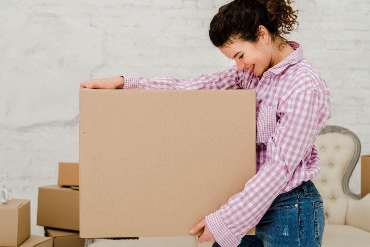 Mujer sonriente con camisa a cuadros carga una caja de cartón plana de gran formato