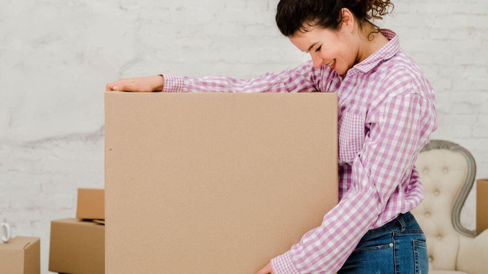 Mujer sonriente con camisa a cuadros carga una caja de cartón plana de gran formato