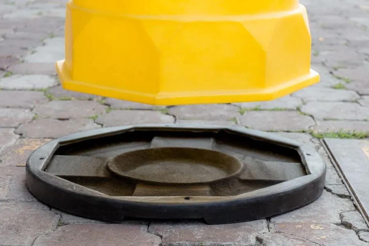 Trafitambo amarillo a punto de asentarse en su base negra, que se ve vacía por dentro, sobre piso de adoquín