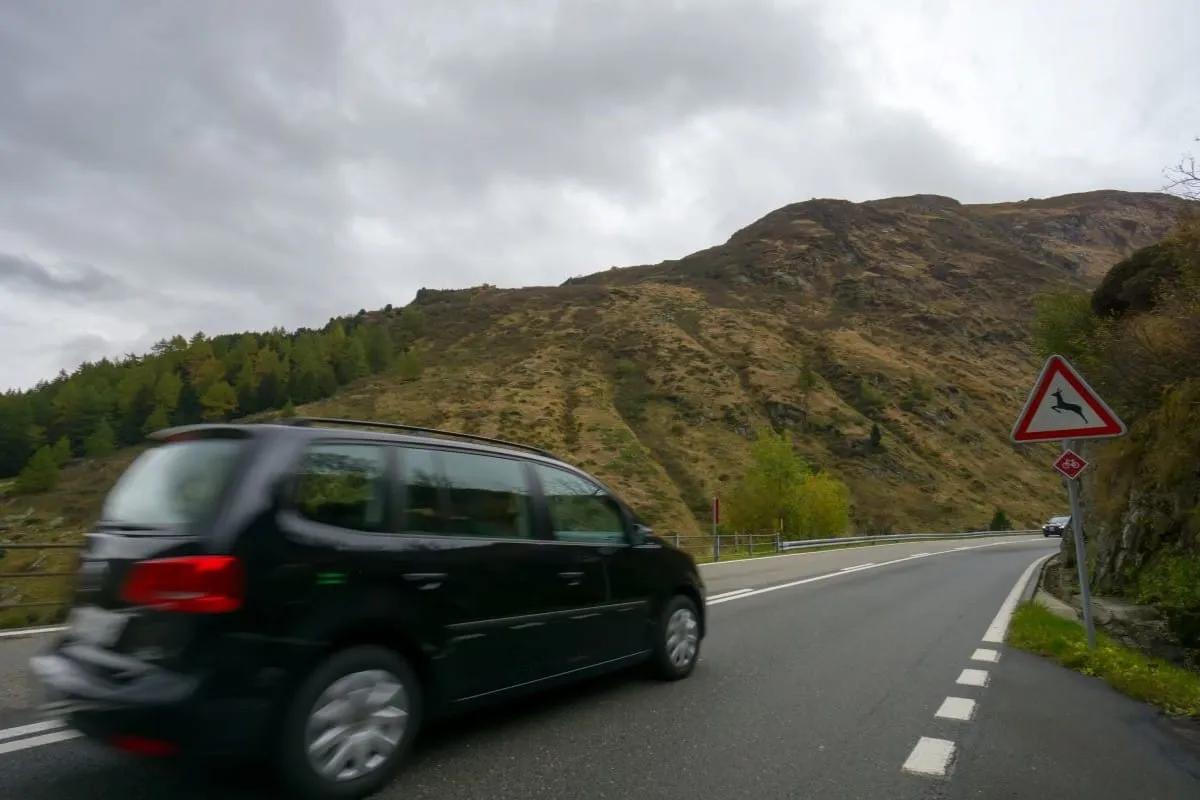 Auto negro en una carretera de montaña junto a una señal triangular de cruce de venados