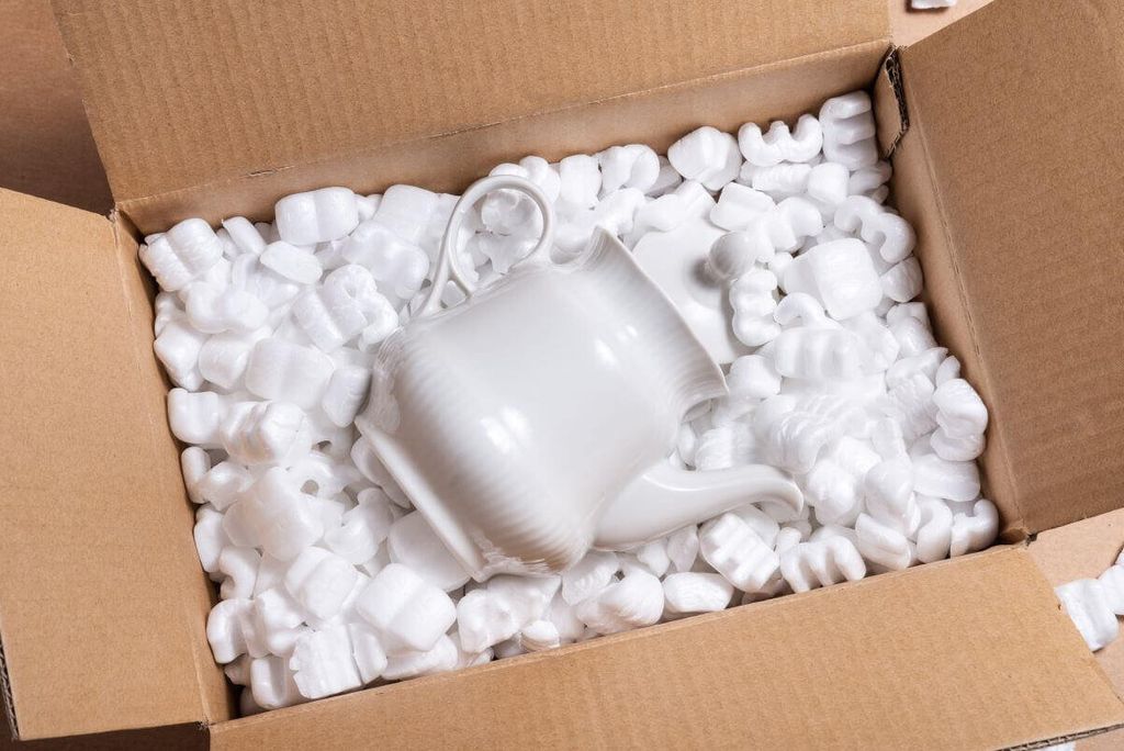 Tetera de porcelana blanca dentro de una caja de cartón llena de cacahuates de relleno blancos