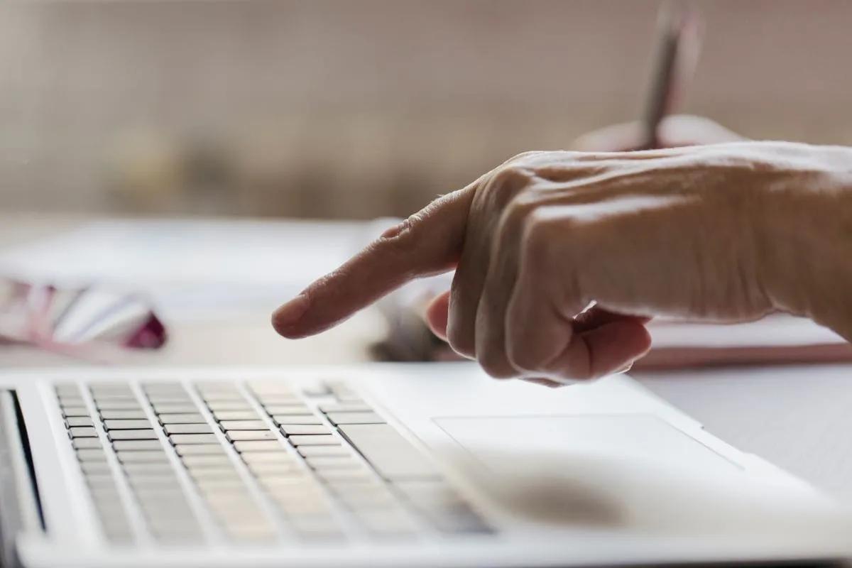 Mano a punto de usar el teclado de una laptop blanca sobre un escritorio