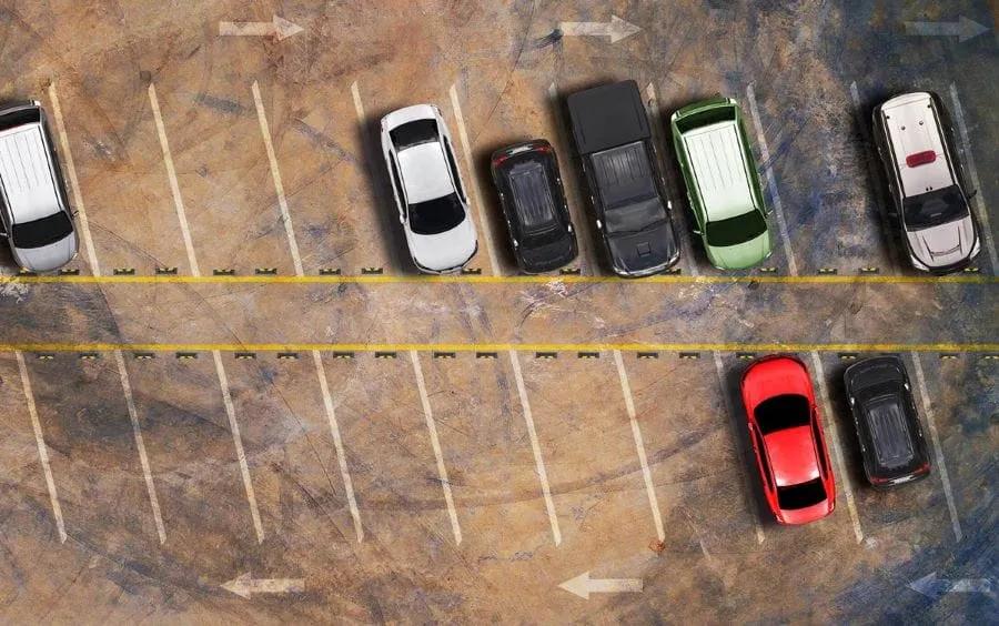 Vista aérea de un estacionamiento con autos en cajones marcados y flechas de circulación en el piso