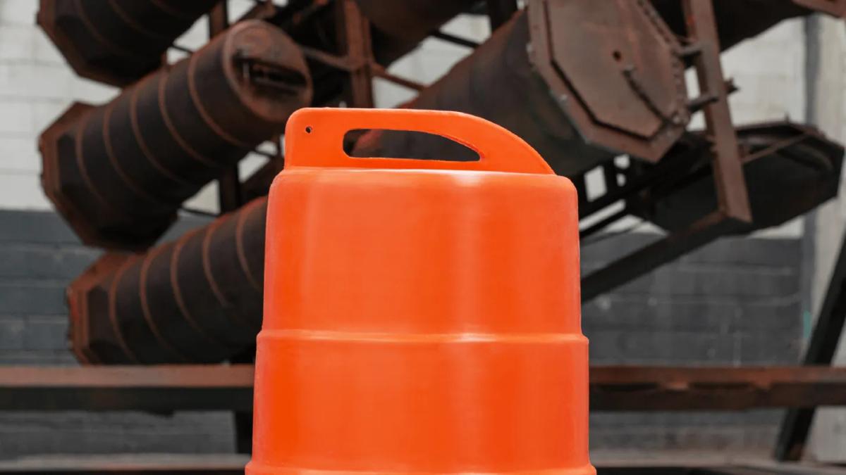 Parte superior de un trafitambo naranja con asa integrada, frente a estructuras metálicas oxidadas