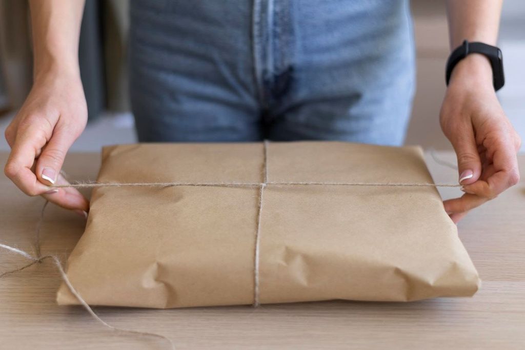 Manos atan con hilo de yute un paquete envuelto en papel kraft sobre una mesa de madera