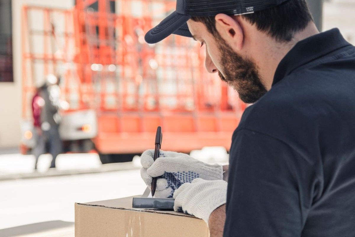 Repartidor con guantes escribe sobre una caja de cartón con una pluma