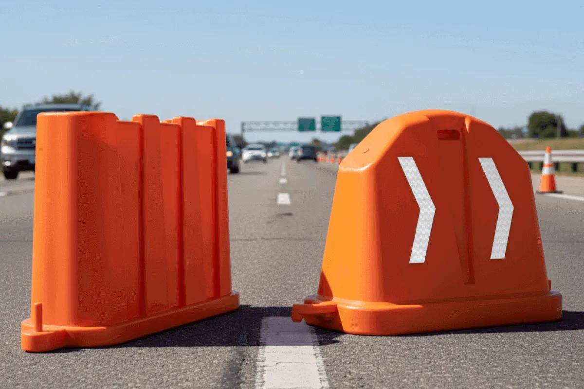 Dos barreras viales anidables naranjas de diseños distintos sobre el carril de una autopista, una con flechas reflejantes
