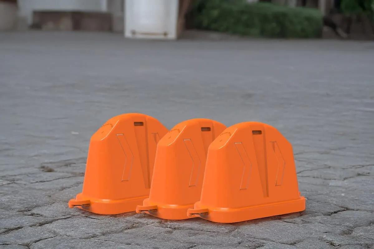 Tres barreras viales anidables naranjas sin reflejantes, una junto a otra sobre un piso de adoquín