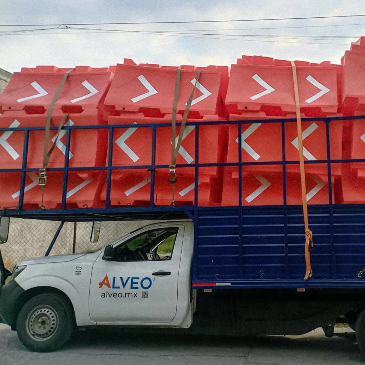 Camioneta de Alveo cargada con barreras viales naranjas con flechas blancas, sujetas con cinchas