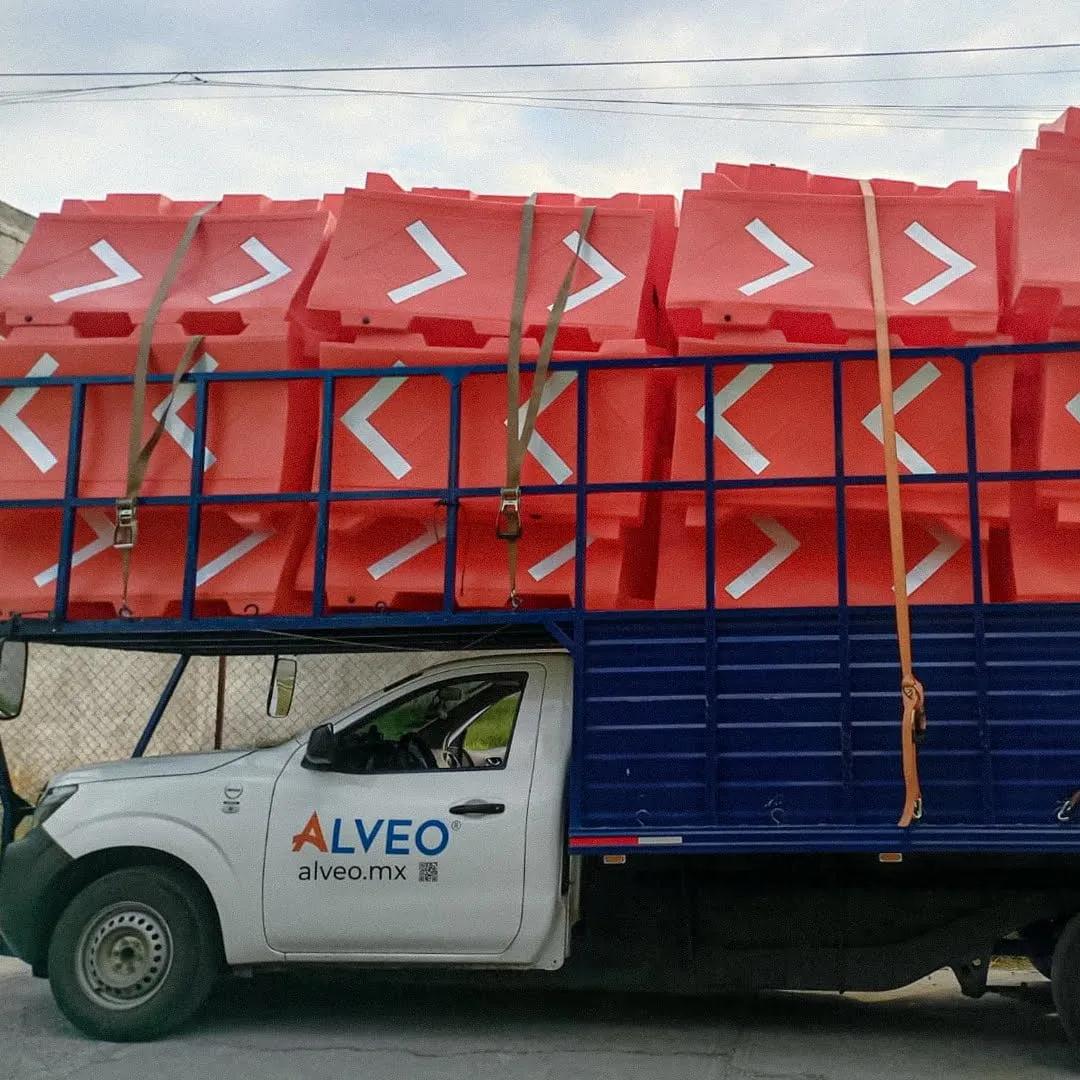 Camioneta de Alveo cargada con barreras viales naranjas con flechas blancas, sujetas con cinchas