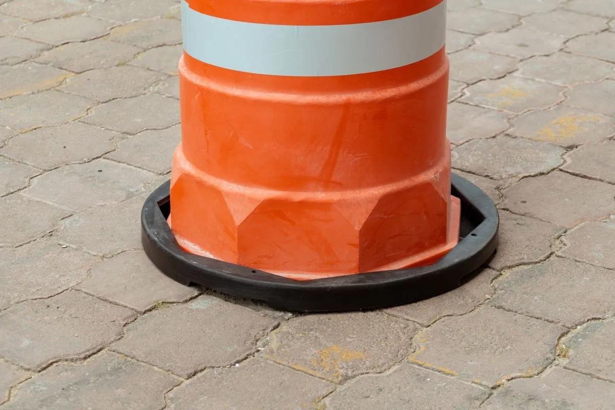 Parte inferior octagonal de un trafitambo naranja montado en su base negra enroscable sobre piso de adoquín