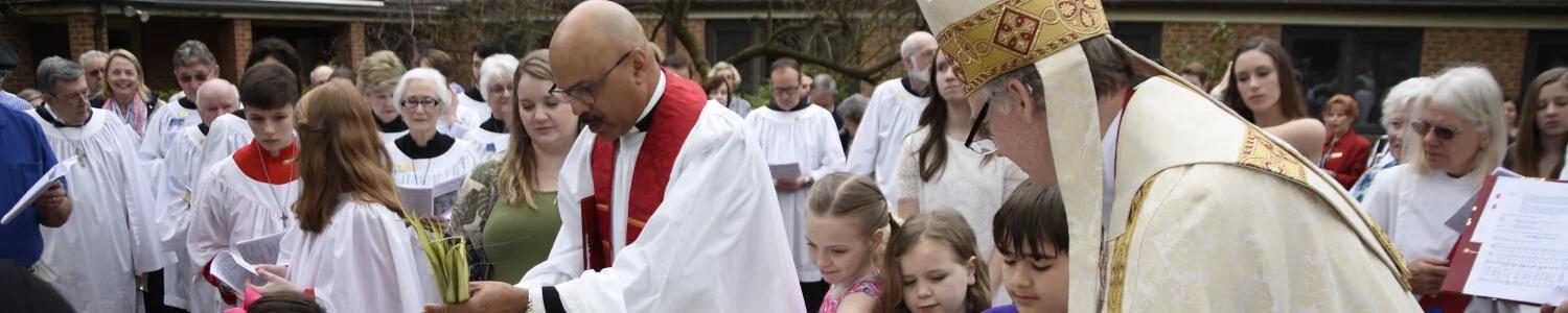 People in church robes and a bishop or priest with children and adults gathered outdoors