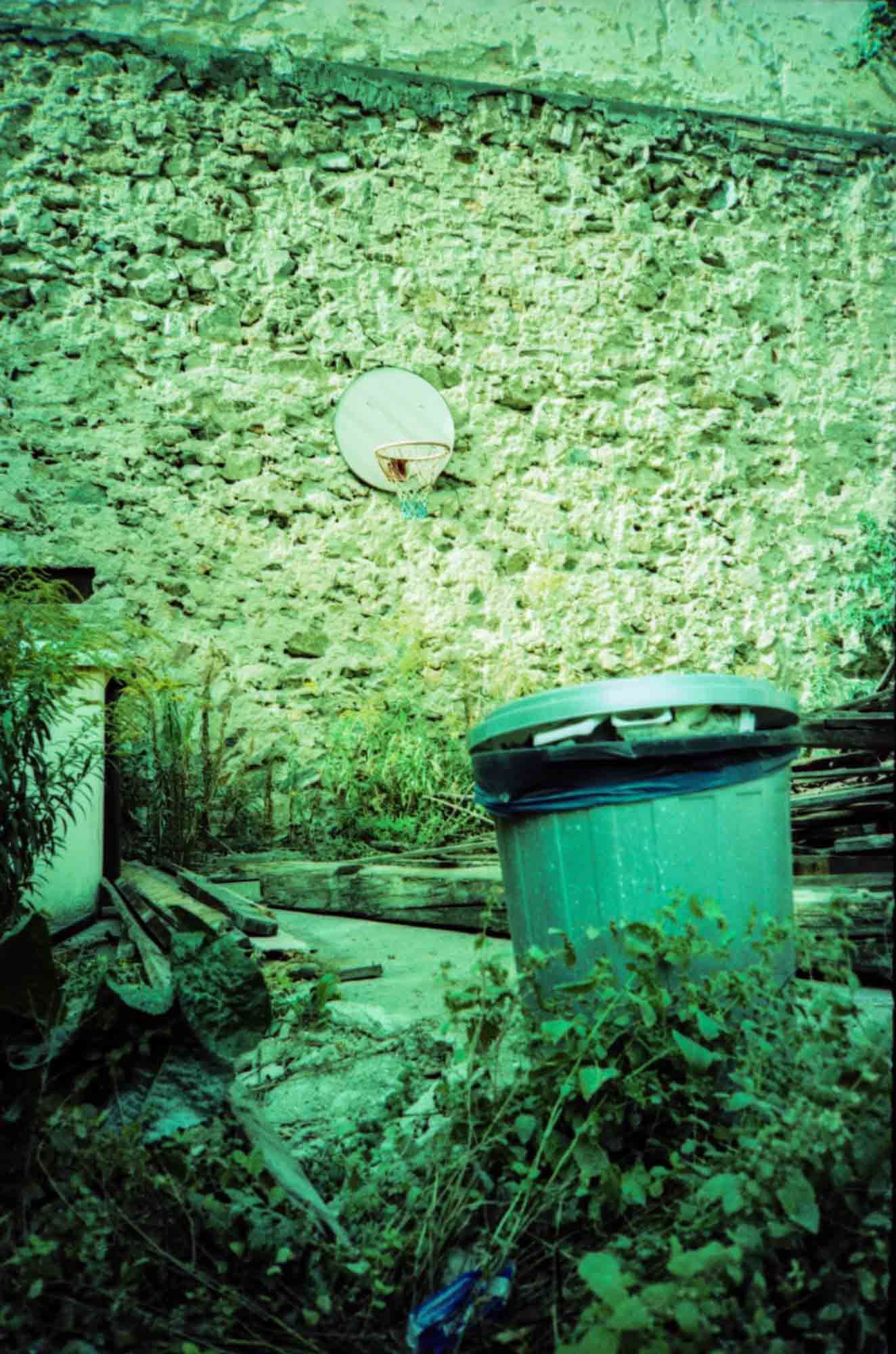 Backyard with basketball basket on the wall and a garbage in the foreground.