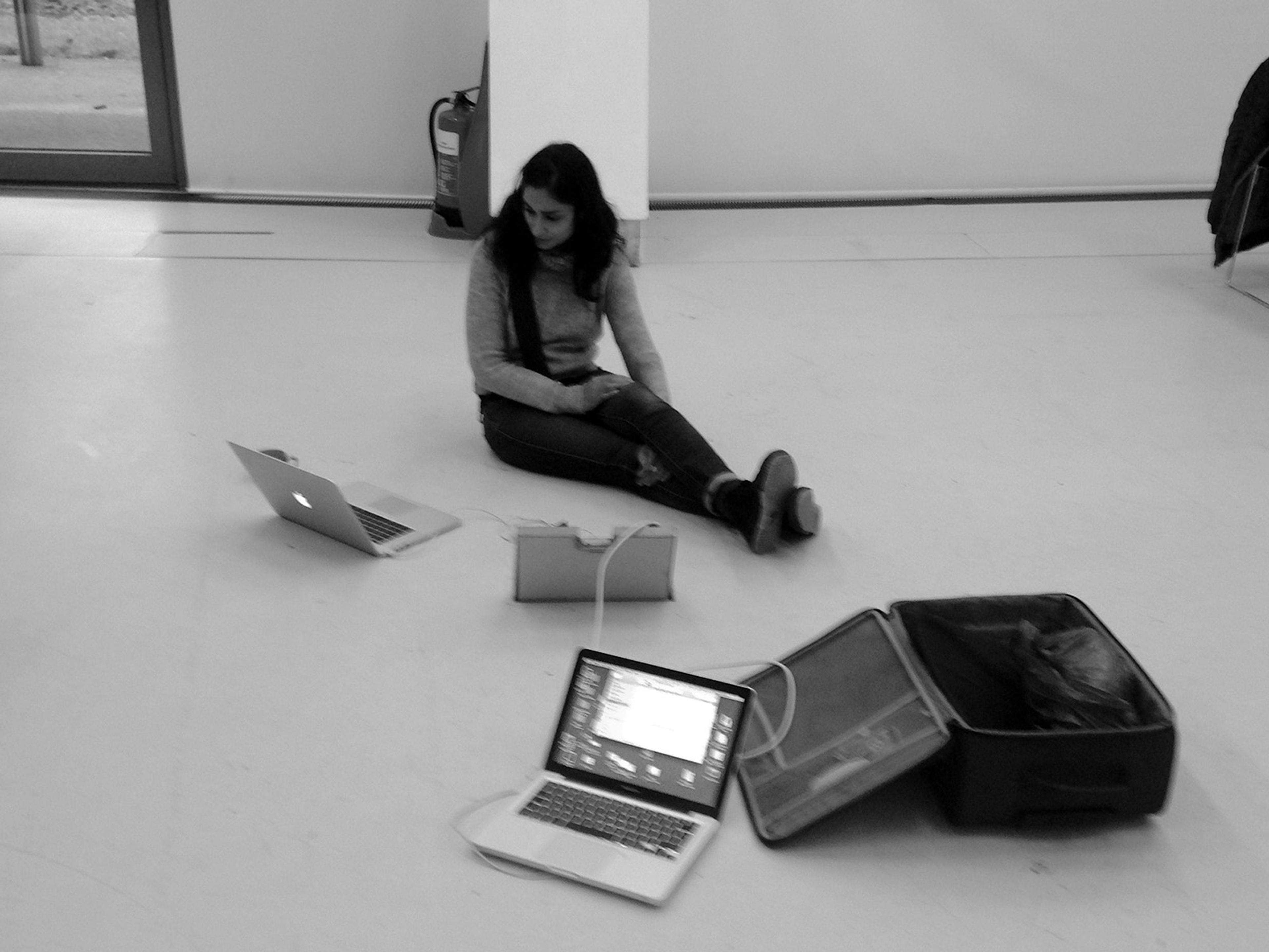A woman sat on a floor with two laptops and an open suitcase