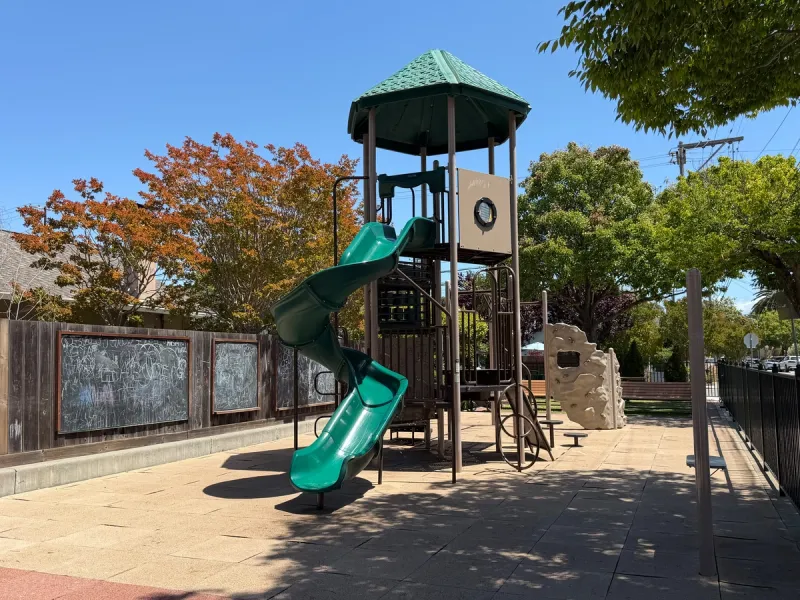 Big kids play equipment consists of just a tall slide, monkey bars and rock wall behind, and not much else