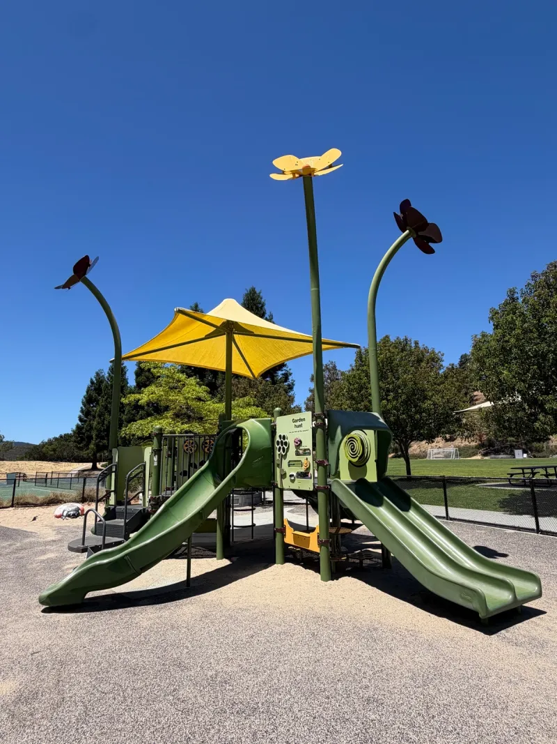 Garden themed toddler play structure complete with flowers looming above