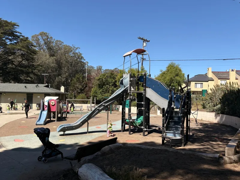 Tall playground structure is next to a toddler sized playground structure