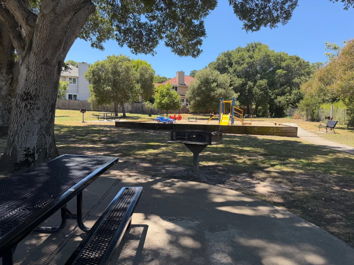 Shaded picnic tables with bbq in front of playground