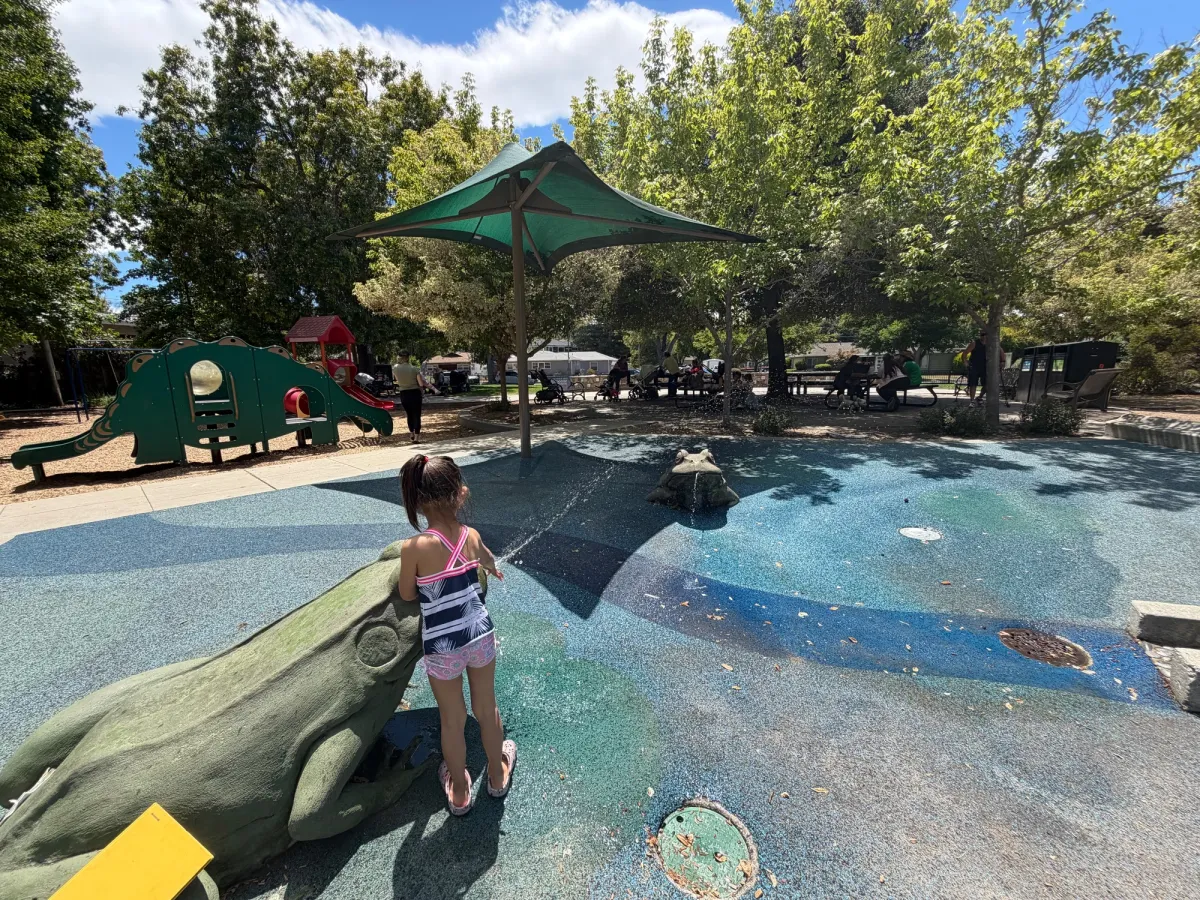 Cluster of picnic tables under shade where nannies/parents gather with a good view of toddler play and splash pad area