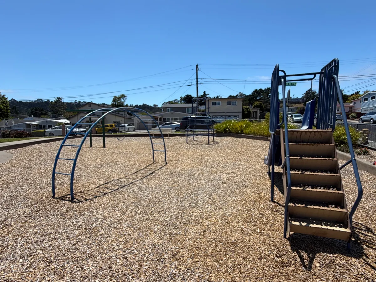 Chain link fence enclosure around park - 1 slide, 2 climbing structures, and swings in the back