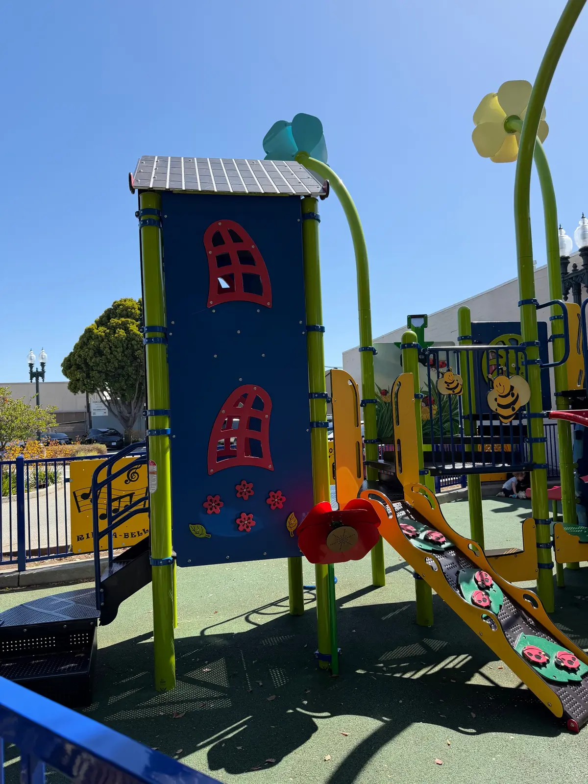 Backside of toddler playground with a ladybug ramp up to the colorful house play structure