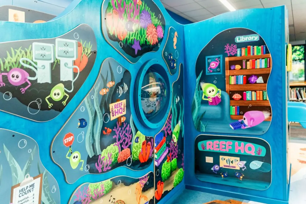 Close up view of the artwork on the play structure. Swimmer bots play underwater around a porthole window. Photo: Santa Clara County Library District.