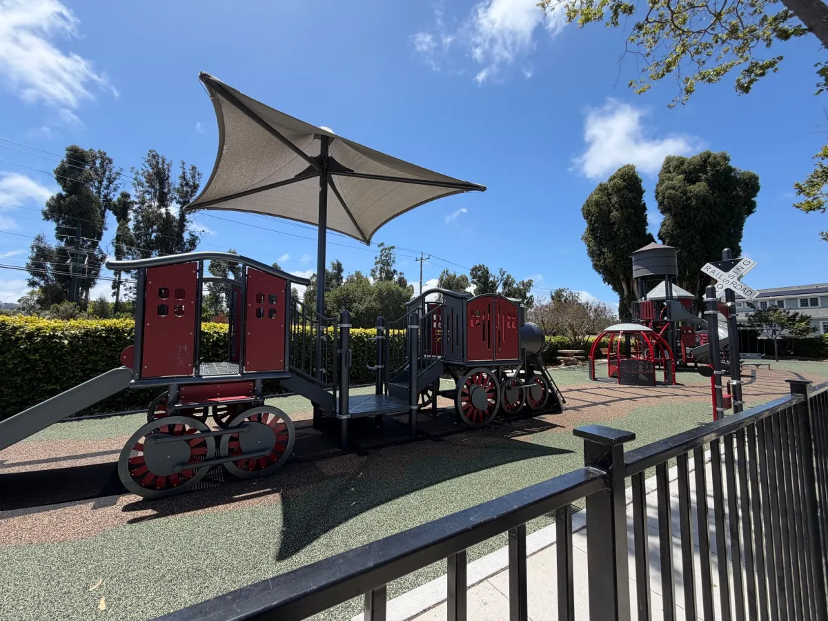 Train shaped play structure on the railroad crossing tracks, and carousel in the back