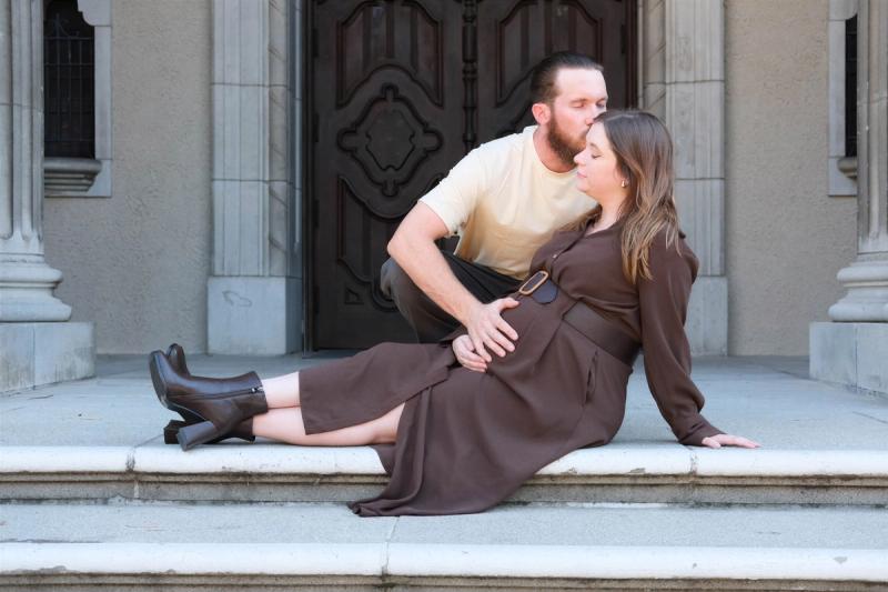 Young couple seated on stone steps, he leans in to kiss her cheek