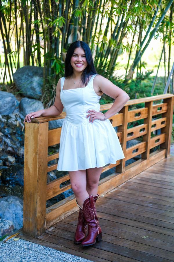 Graduate in a white dress and cowboy boots on a wooden garden bridge
