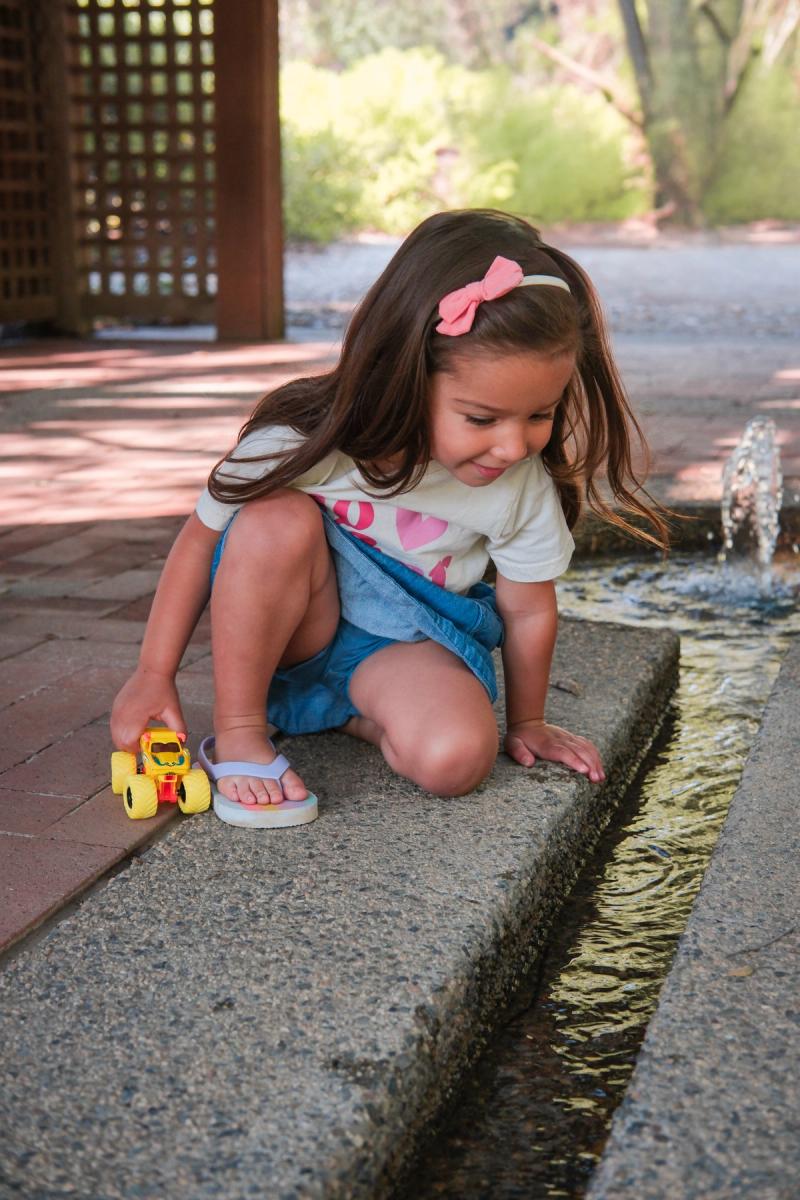 Little girl in a pink bow sitting beside a garden water channel