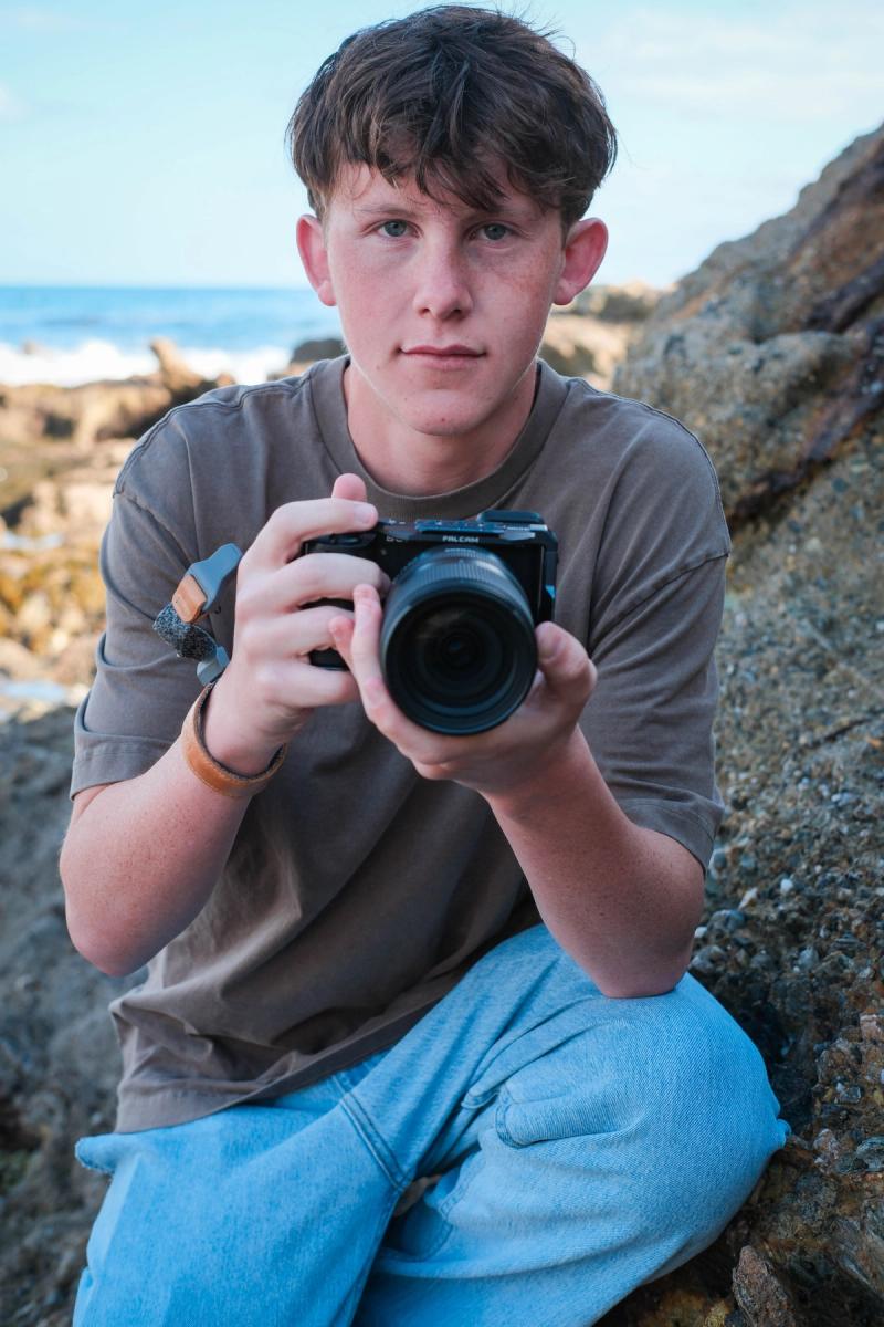 Smiling teen photographer holding his camera while kneeling on the rocks