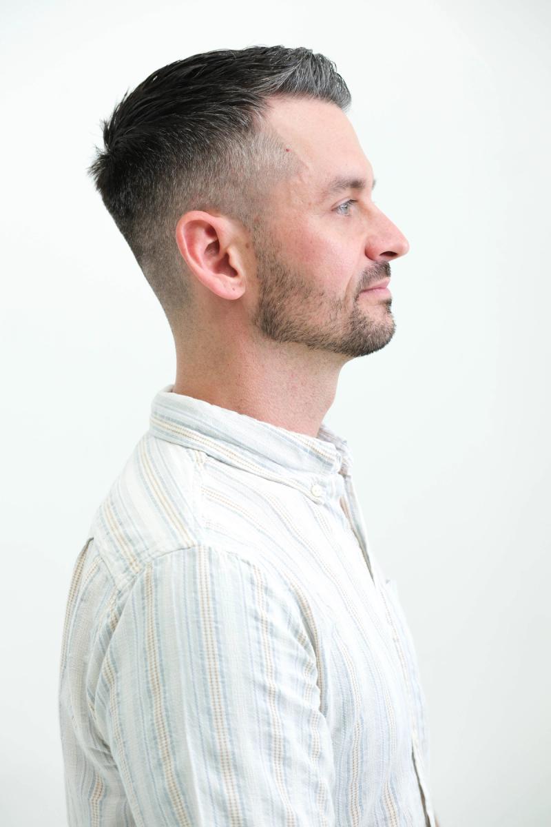 Profile portrait of a man in a light striped shirt against a white backdrop